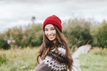 Beautiful carefree long hair asian girl in the red hat and knitted nordic sweater in autumn nature...