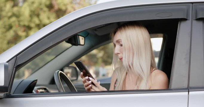 Beautiful blonde woman using her smartphone in seat of car looked at the camera and smiled.