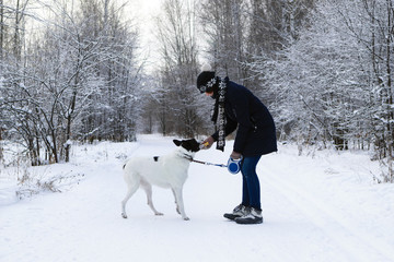 Young woman is playing with her black-white dog on a walk in winter forest.