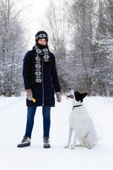 Portrait of beautiful smiling young woman with her black-white dog on a background of winter forest.