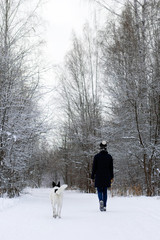 Young woman is walking with her black-white dog in winter forest.