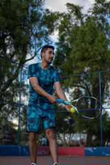 Hombre adulto latino con barba de camiseta azul en pantaloneta jugando tenis  con amigo en cancha profesional  hispano