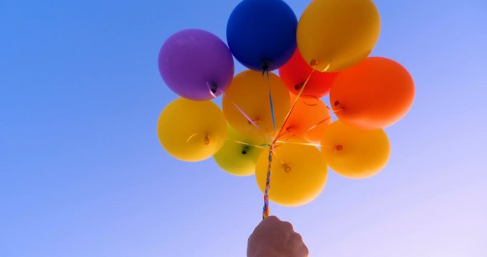 A large bunch of yellow Helium ballons straining on their strings against a sunny sky with white clouds, A lot of flying balloons with helium in blue sky with clouds.