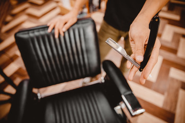 Barber hairdresser holds razor on background chair, beauty salon for men