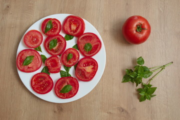 Directly above shot of the sliced tomato with basil on the plate against the wooden background