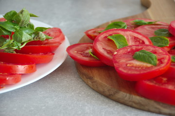 Closeup shot of the sliced tomato with basil on a plate and cutting board