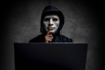 Hacker wearing a white mask in front of his computer. hacker hacks network, Space for text.