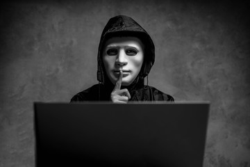 Male hacker hidden face with the mask accessing to personal information on laptop in the dark....