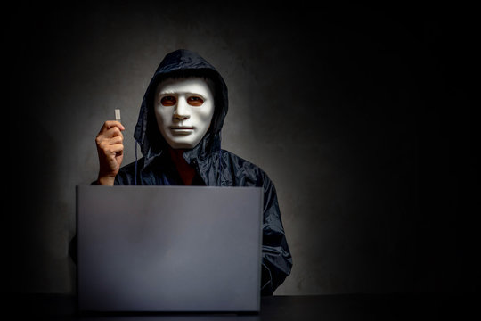 Male hacker hidden face with the mask and hoodie. Obscured dark face holds a USB flash drive in his hands, Data thief, internet attack, darknet and cyber security concept, with copy space