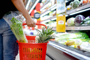 Closeup Young women hand holding the basket for shopping of fruit and vegetables in Supermarket store bokeh background