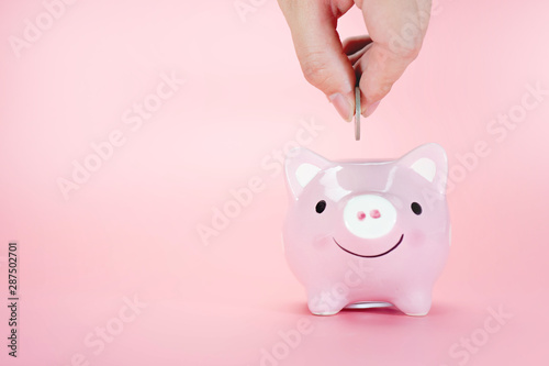 Hand Putting Coin In Piggy Bank On A Pink Background Saving - 