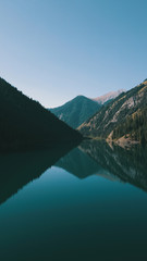 Kolsay lake located in the mountains of Kazakhstan. Turquoise water as a mirror. The water reflects the mountains, green hills, tall spruce, grass, sky and clouds. Beautiful landscape of mountain lake