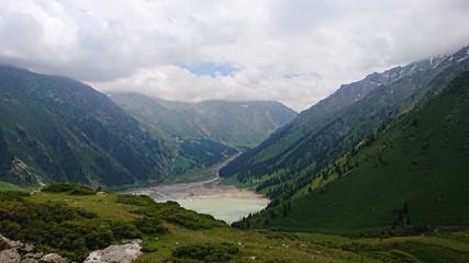 Big Almaty lake located in the mountains of Kazakhstan. It offers views of green grass, flowers, lake, rocks, large mountains and the sky in the clouds. Mountain lake with blue water.