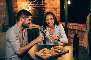 romantic couple making a toast while eating pizza at home backyard, evening scene