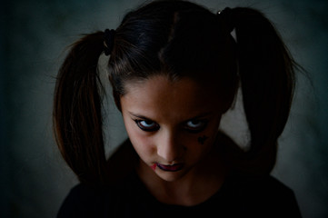 young little caucasian girl with pigtails with dark gothic makeup looking angry during Halloween holiday party looks like movie character