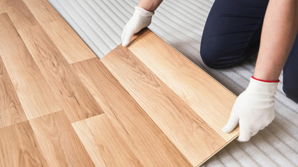 Installing laminated floor, detail on worker hands in white gloves fitting wooden tile, over white...