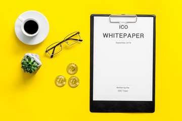 White paper ICO, coins, glasses, coffee on yellow background top view
