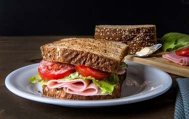 Sandwich on a white plate with lettuce ham tomato cheese and mayo.  Bread and a soon with mayo on the background