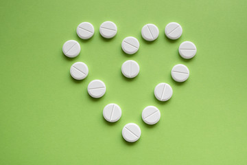 Heart sign made of medicine pills on a green background. Isolated.