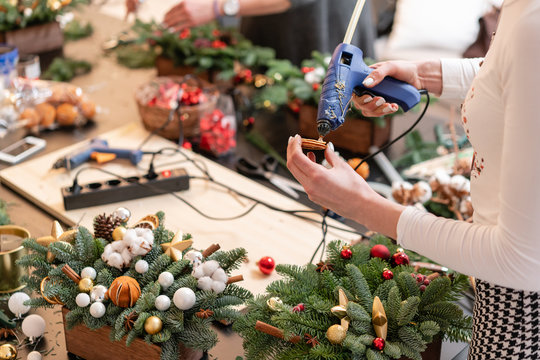 Glue Gun In Woman Hand. Manufacturer Of Christmas Wreath From Branches Of Pine For Holiday. Master Class On Making Decorative Ornaments.