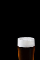 Beer with foam in a tall glass against black background