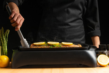 Chef cooking, seafood, red fish grills with smoke, salmon or trout on a black background. Movement, Restaurant menu, recipe book, Asian cuisine, homemade recipe. Horizontal photo