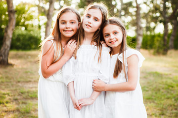 Three girls in white dresses walk in nature in the summer. Children's pastime during the summer...
