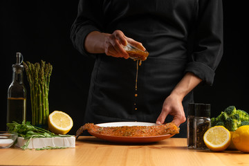 Chef watering seafood, red salmon fish or trout marinade juice, Asian cuisine, a recipe book, on a black background. Preparing tasty and healthy food.