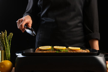Chef cooking, seafood, red fish grills with smoke, salmon or trout on a black background. Movement, Restaurant menu, recipe book, Asian cuisine, homemade recipe. Horizontal photo