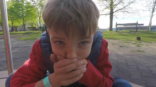 boy rides on a carousel, shows that he is ill, closes his mouth with his hands
