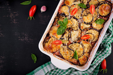 Baked eggplant with cheese on a dark wooden table. Parmigiana melanzane. Top view. Italian cuisine....