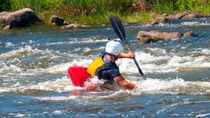 Playboating. A man sitting in a kayak with oars in his hands performs exercises on the water. Kayaking freestyle on whitewater. Eskimo roll.