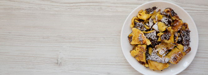 Homemade german Kaiserschmarrn pancake on a white plate on a white wooden surface, view from above. Flat lay, top view, overhead. Copy space.