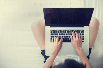Young woman drinking coffee at home in her bed and checking her laptop
