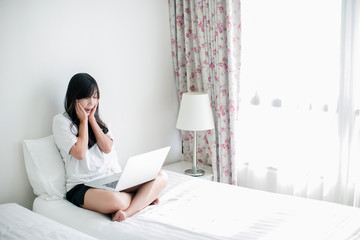 Young woman drinking coffee at home in her bed and checking her laptop