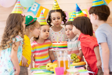 Group of adorable kids 3-5 years gathered around festival table. Children blow out candles on cake. Birthday party for preschoolers