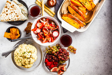 Flat lay of vegan food: baked sweet potato, cauliflower, fruits, vegetable salad and tortilla with greens on white background.