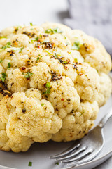 Whole baked cauliflower with spices on gray plate. Healthy vegan food concept.