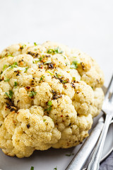 Whole baked cauliflower with spices on gray plate. Healthy vegan food concept.