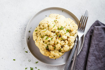 Whole baked cauliflower with spices on gray plate. Healthy vegan food concept.