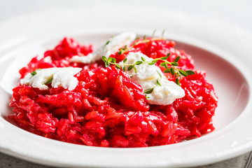 Pink beetroot risotto with feta cheese in white plate.