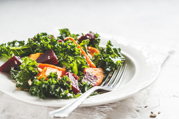 Kale salad with baked vegetables in white plate.