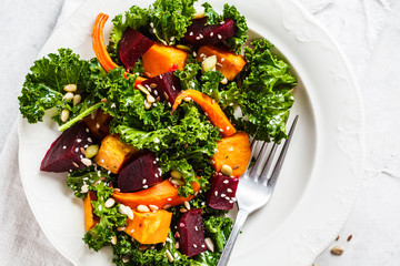 Kale salad with baked vegetables in white plate.