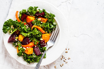 Kale salad with baked vegetables in white plate.