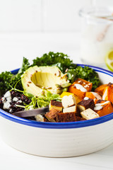 Buddha bowl salad with black rice, avocado, tofu, sweet potato, kale and tahini dressing, white background.