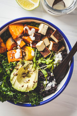 Buddha bowl salad with black rice, avocado, tofu, sweet potato, kale and tahini dressing, white background.