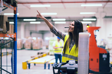 Female forklift operator with headset communication equipment showing location on the shelf to...