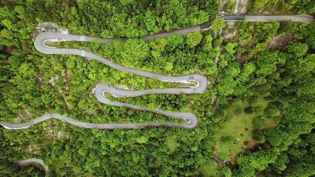 Drone footage of curvy mountain side roads with traffic driving through them surrounded by green pine tree forest hills near Trenta Slovenia, Europe in Triglav National Park