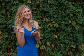 Young beautiful girl on a background of a wall of wild grapes, makes notes in a notebook, an idea has come. Copy space.