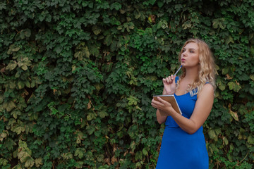 Young beautiful girl on a background of a wall of wild grapes, makes notes in a notebook, an idea has come. Copy space.